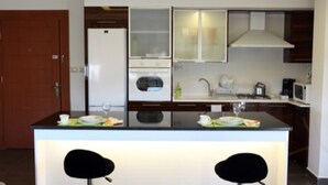 A modern kitchen with a central island, two black bar stools, a refrigerator, oven, microwave, and a sink. - Eco Two bed Apartment With Roof Garden in Amman (Amman)