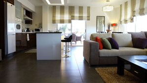 A modern kitchen with a central island, a dining area with chairs, and a living room with a sofa and cushions. - Eco Two bed Apartment With Roof Garden in Amman (Amman)