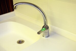 Un lavamanos con grifo cromado y una etiqueta verde que indica ahorro de agua.