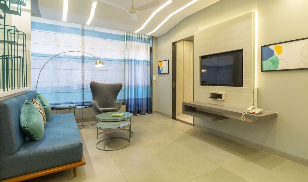 Una sala de estar moderna con sofá, sillón y mesa de centro, un televisor de pantalla plana montado en la pared, y un ventanal con cortinas.