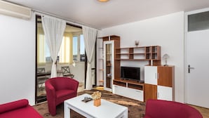 Ein modernes Wohnzimmer mit roten Möbeln, einem weißen Couchtisch und einem Fernseher auf einem Holzregal.