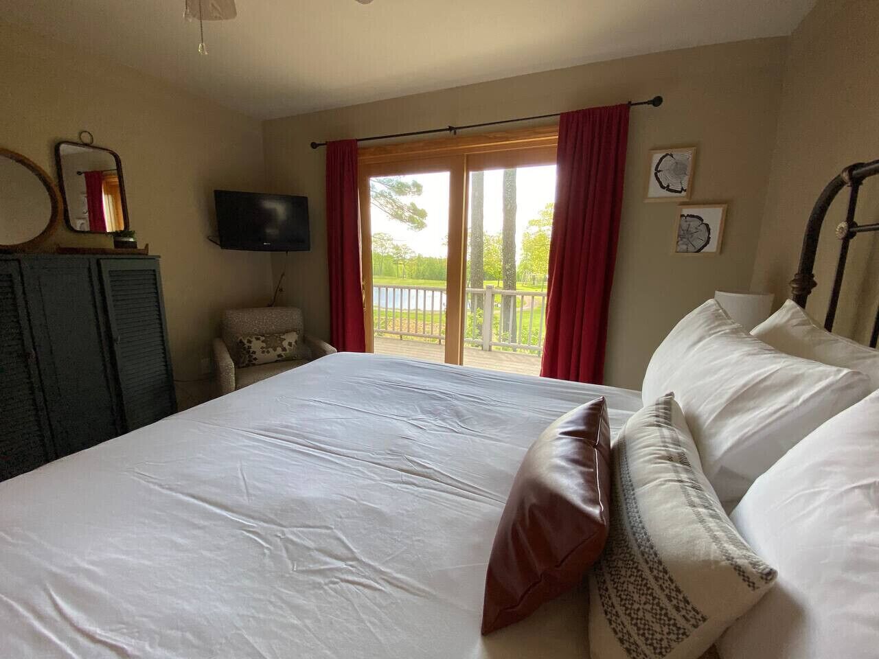 A bedroom with a large bed, a television, a desk, and a window with red curtains.