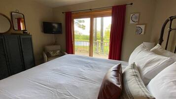 A bedroom with a large bed, a television, a desk, and a window with red curtains.