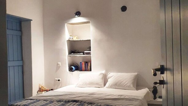 A bedroom with a bed, a shelf unit, and a blue door.