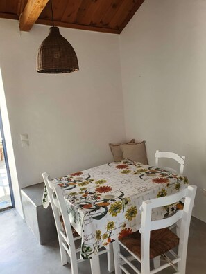 A dining area with a table covered in a floral tablecloth, white chairs, and a hanging light fixture. - 2 Tiny houses for 2 couples or Family (Karavas)
