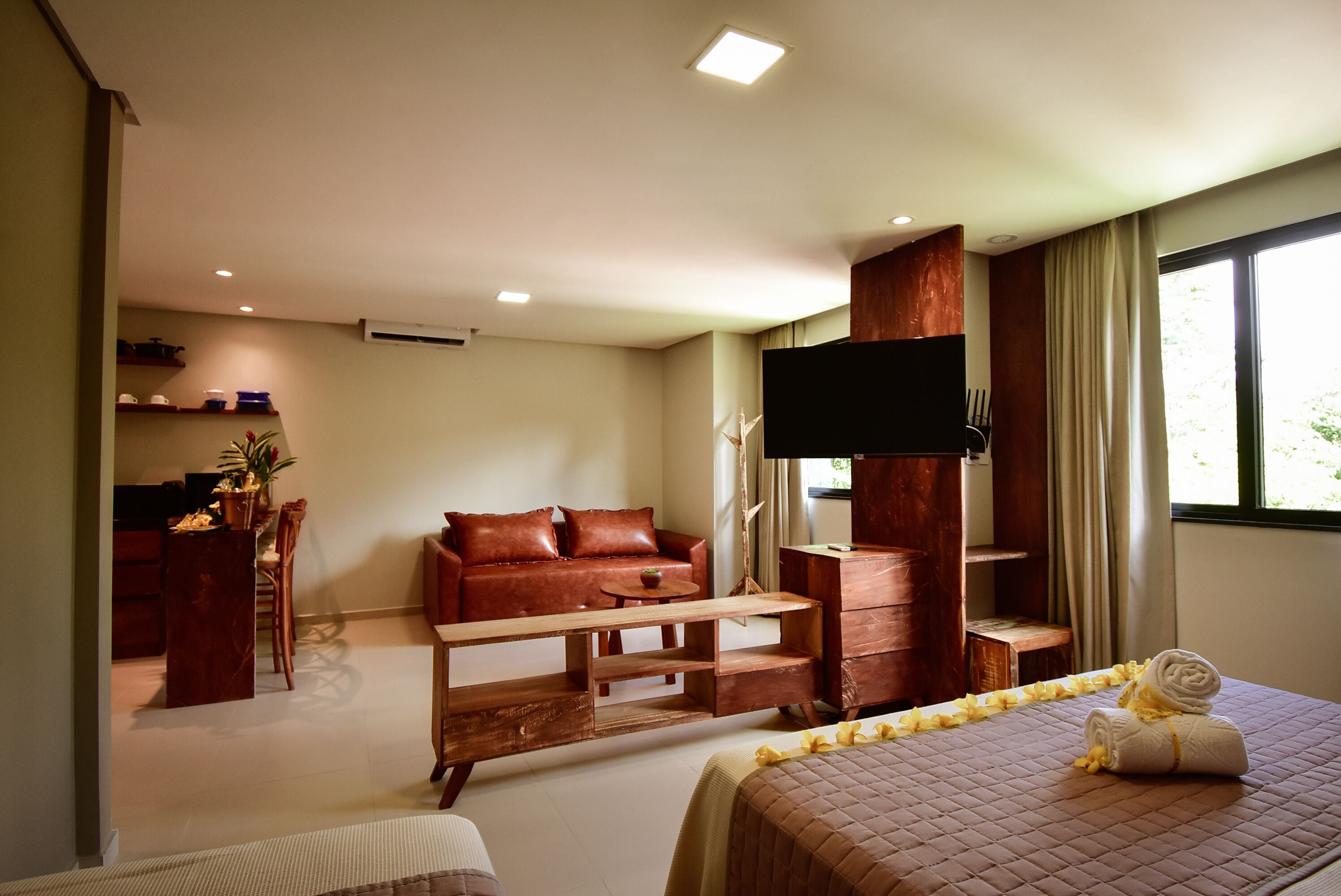 Habitació d'hotel moderna amb llit, sofà, televisió, una banca de fusta i escriptori amb cadira.