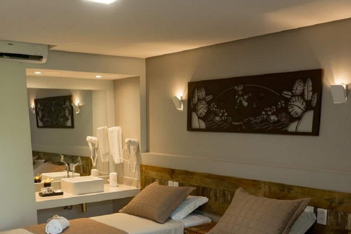 Une chambre d’hôtel avec trois lits simples, un grand miroir, une coiffeuse avec des articles de toilette et un élément décoratif mural.
