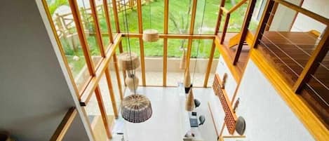 A spacious room with large windows, a wooden staircase, and a view of a garden.