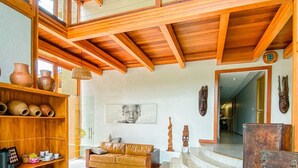 Amplia sala de estar con techo alto, vigas de madera, un sofá, una escalera y una repisa con cerámica.