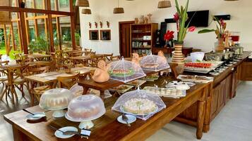 A buffet setup with covered dishes and a dining area with wooden tables and chairs.