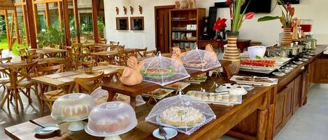 A buffet setup with covered dishes and a dining area with wooden tables and chairs.