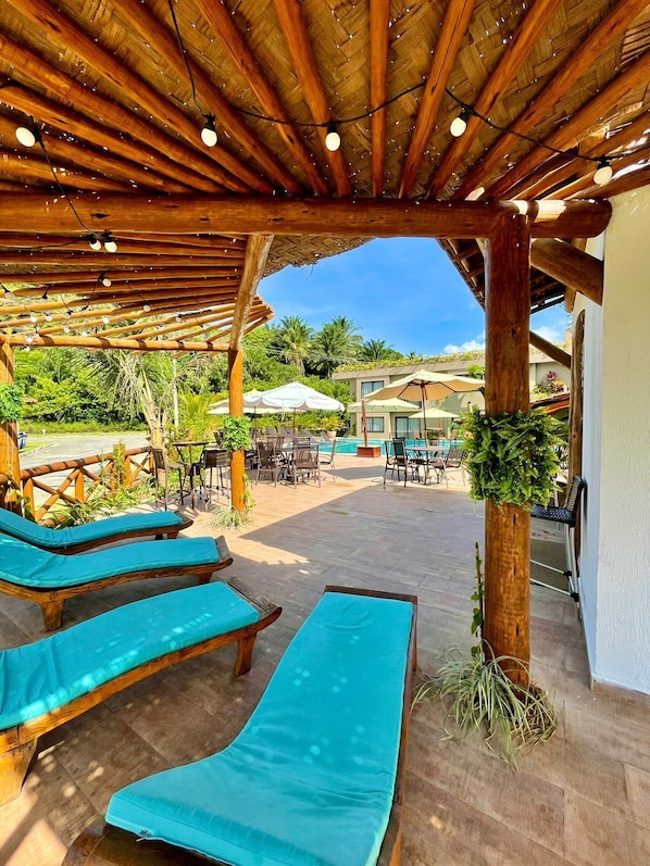 A covered outdoor seating area with wooden loungers and string lights.