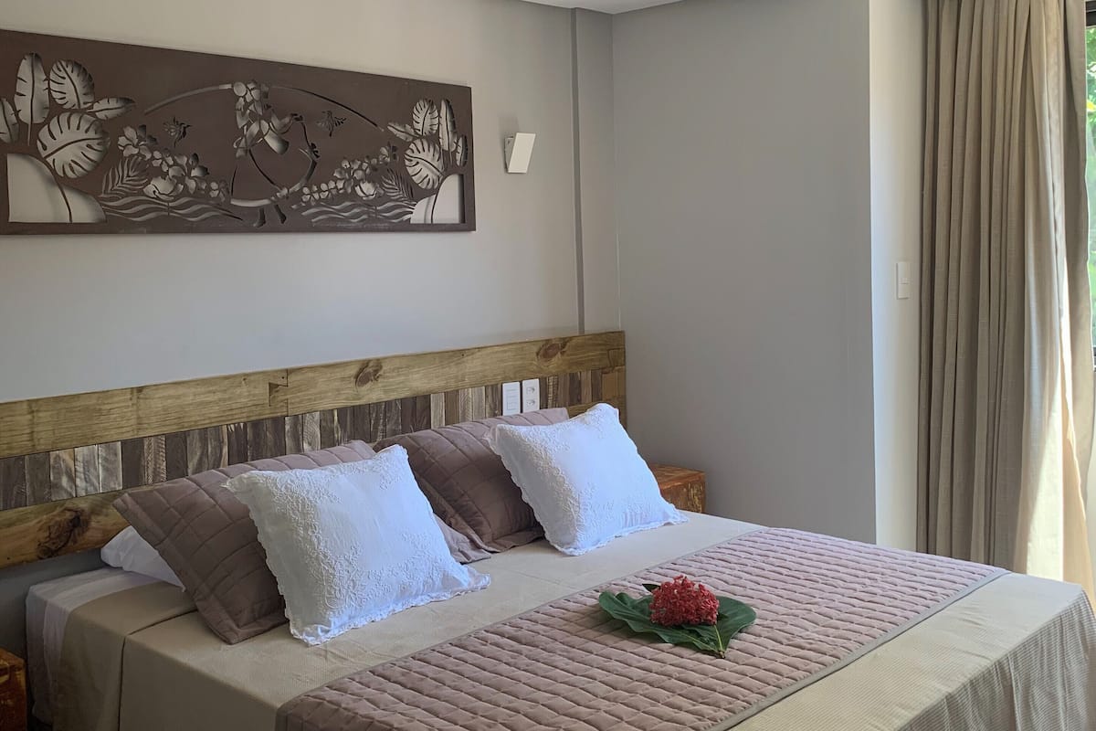 Un lit bien fait, avec une tête de lit en bois, un élément décoratif mural et une fenêtre avec des rideaux.