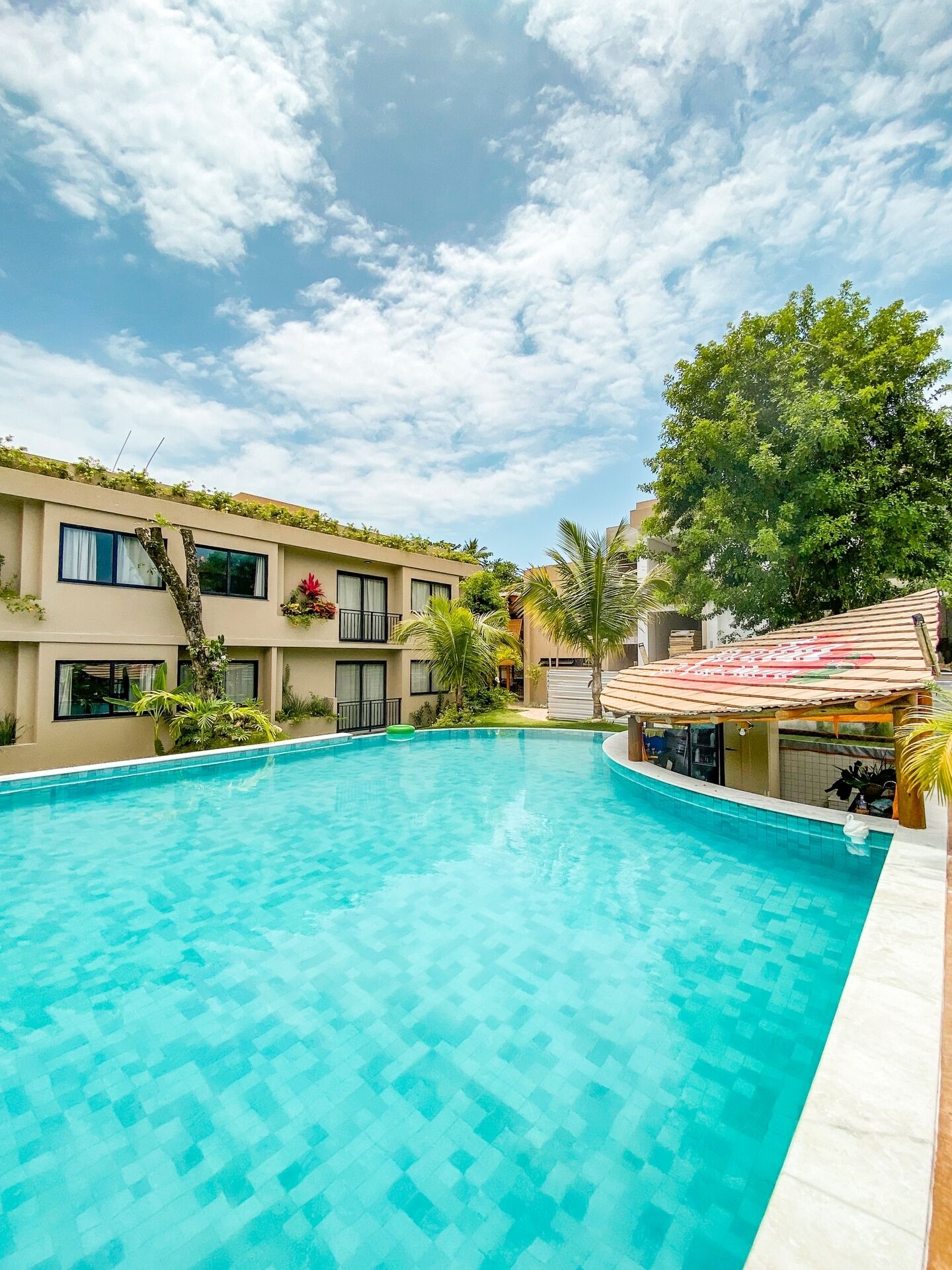 A swimming pool with a tiled deck, surrounded by buildings with balconies and greenery.
