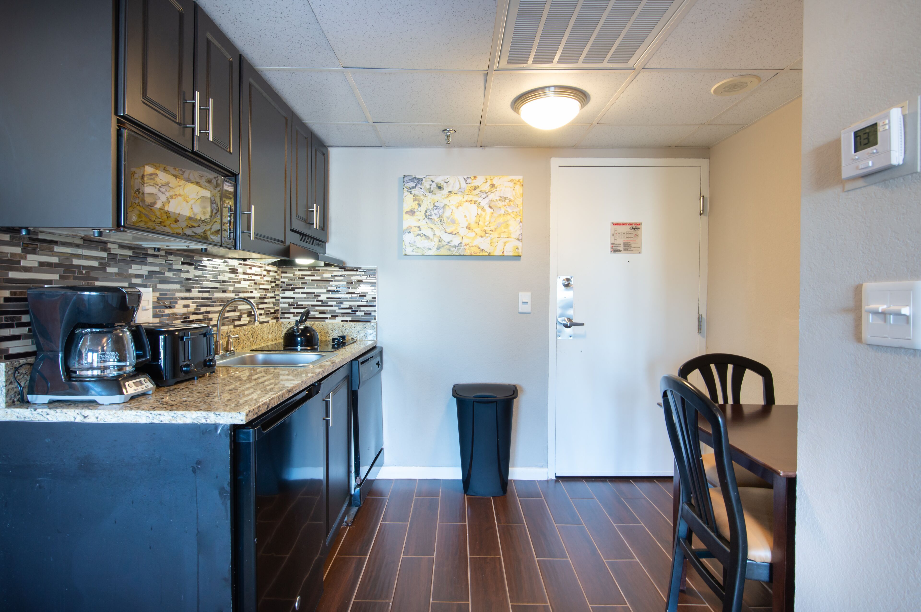 A compact kitchen with dark cabinets, a coffee maker, and a trash bin.
