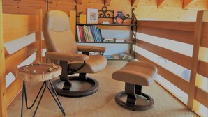 Une pièce chaleureuse aménagée comme une cabane, avec un plafond en bois, un fauteuil confortable, une petite table et une bibliothèque remplie de livres.
