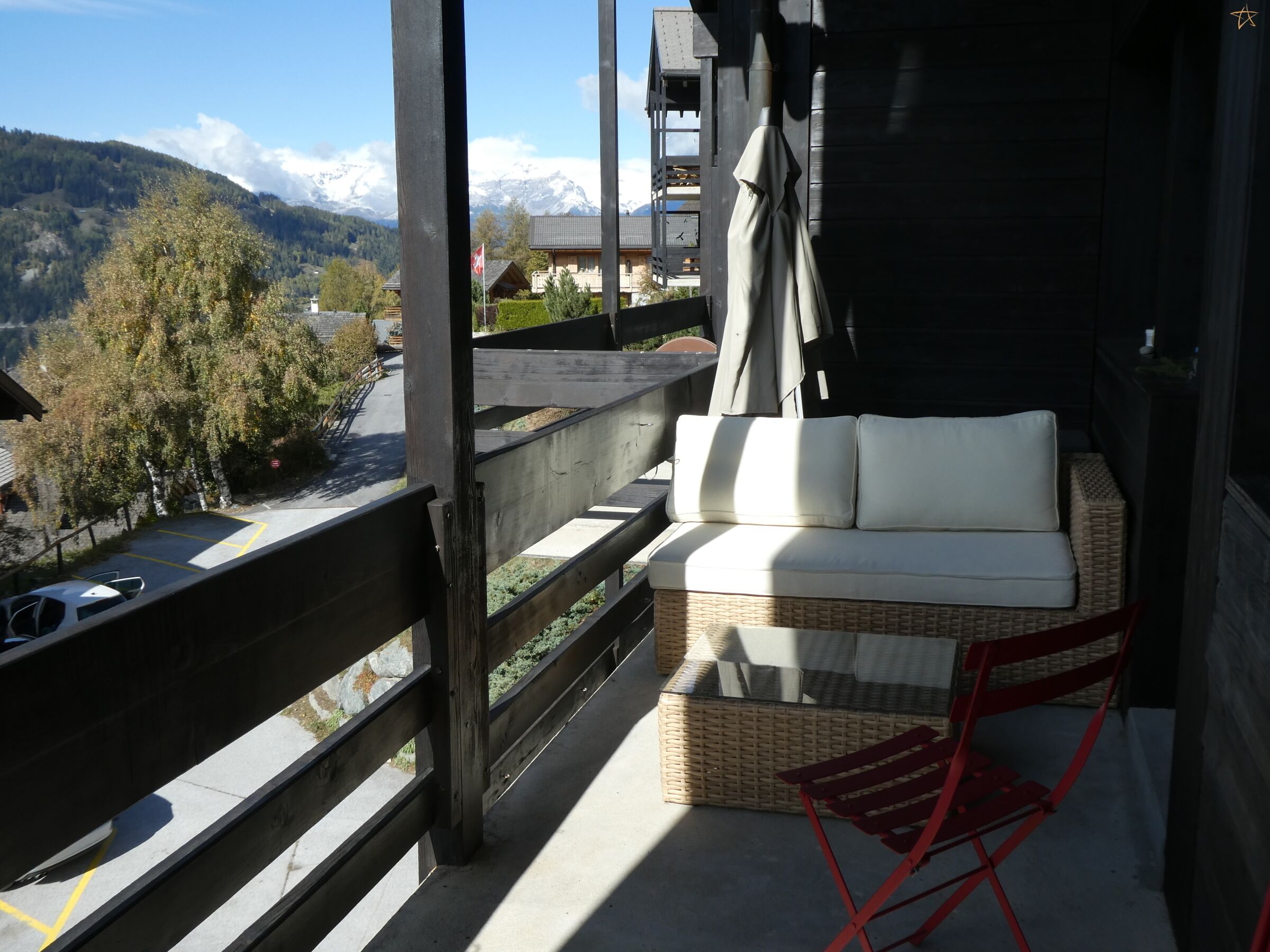 Un balcón con un sofá de mimbre y una silla roja, con vistas a un paisaje montañoso.