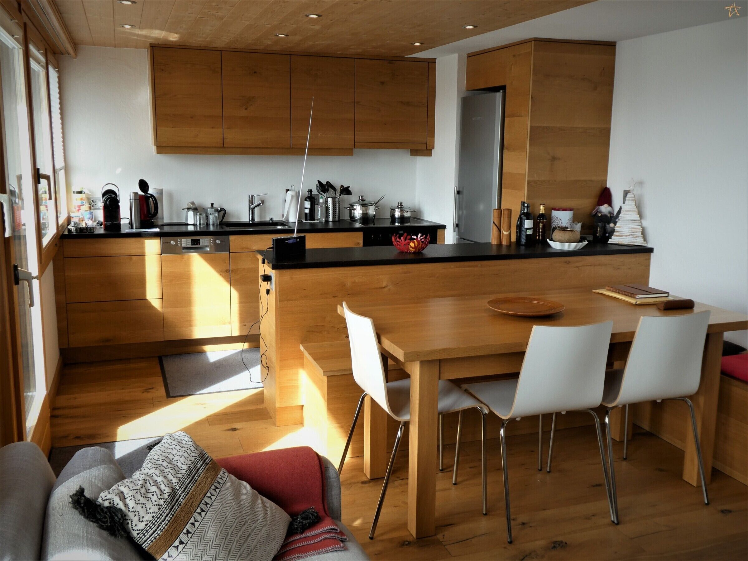A modern kitchen with wooden cabinets, a black countertop, and a dining area with a wooden table and white chairs.