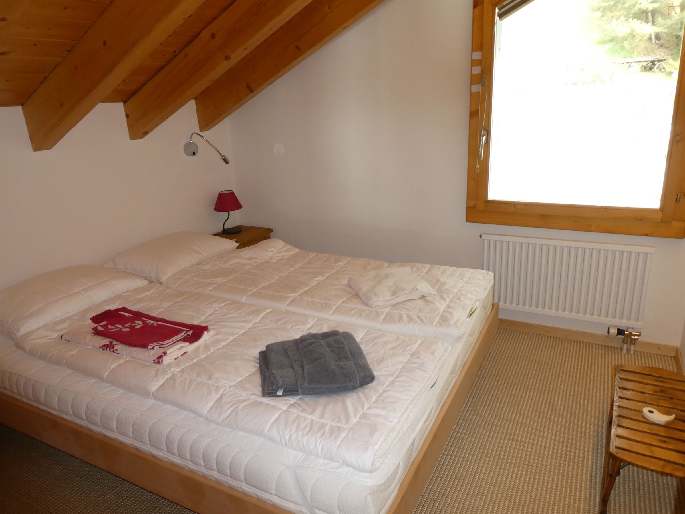 Ein Schlafzimmer mit einem Bett, einem Nachttisch mit Lampe, einem Fenster und einer Heizung.