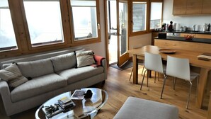 Un espace de vie moderne comprenant un canapé, une table basse en verre, un coin repas avec des chaises et un plancher en bois.
