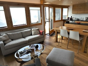 A modern living space with a sofa, a glass coffee table, a dining area with chairs, and wooden flooring.