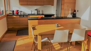 Une cuisine moderne avec des meubles en bois, un plan de travail noir et une table à manger en bois, assortie de chaises blanches.