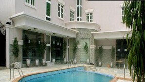 A swimming pool with a stone border, surrounded by a building with multiple windows and outdoor seating areas. - Excel Oriental Hotel & Suites (Lagos)
