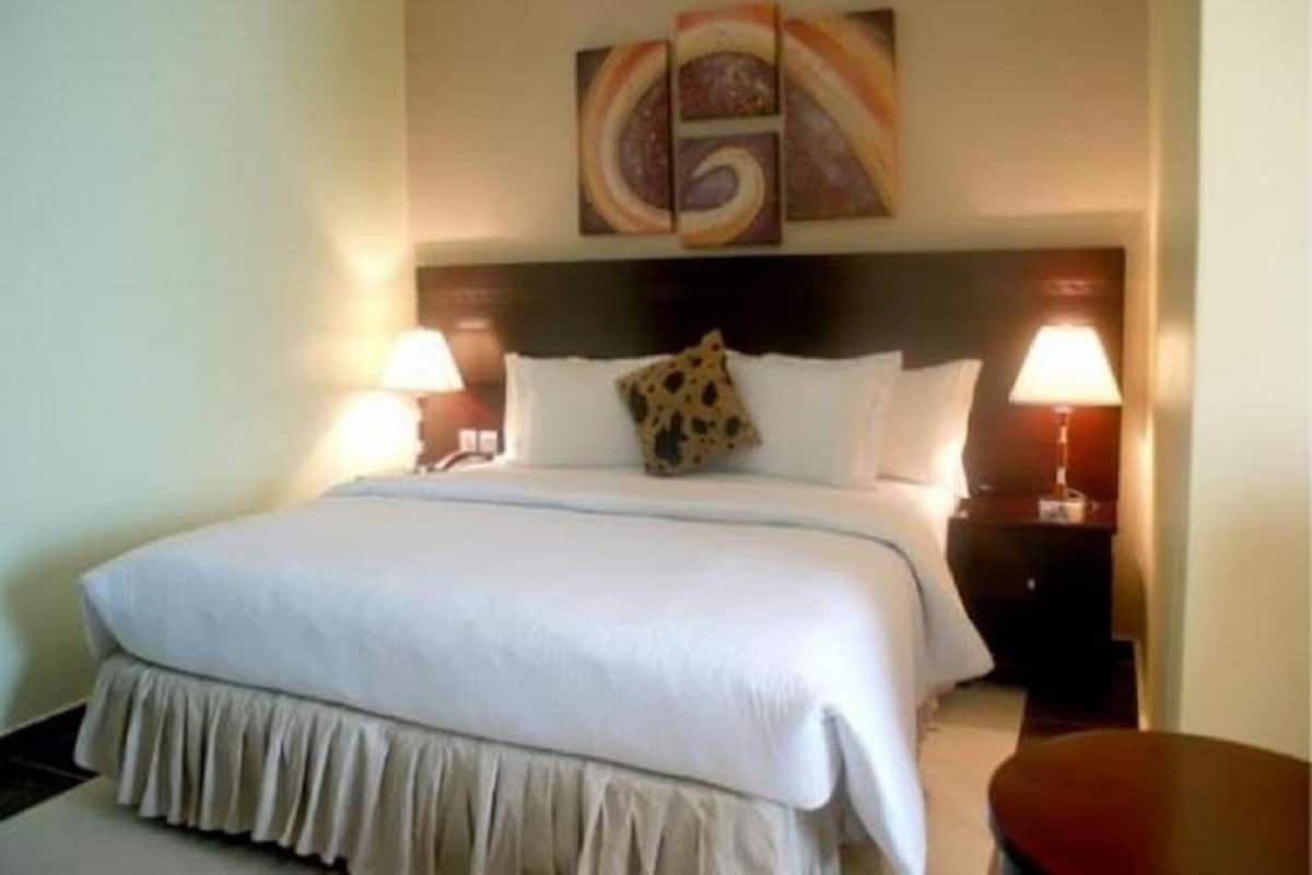 Ein Hotelzimmer mit einem großen Bett, zwei Nachttischlampen, einem Kopfteil mit dekorativer Applikation und einem kleinen runden Tisch.