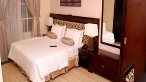A hotel room with a large bed, a bedside table with a lamp, a dresser, and a mirror. - Excel Oriental Hotel & Suites (Lagos)