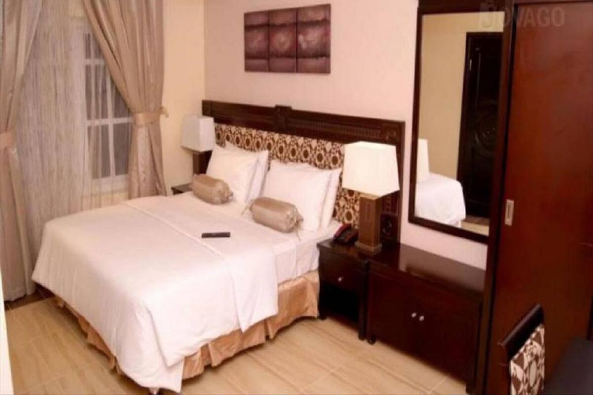 Ein Hotelzimmer mit einem großen Bett, einem Nachttisch mit Lampe, einem Schminktisch und einem Spiegel.