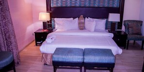 Habitación de hotel con una cama grande, dos mesitas de noche, una silla y un cabecero estampado.