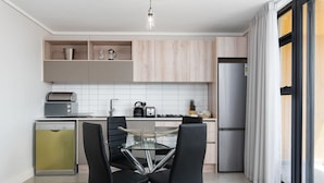 Una cocina moderna con comedor, que incluye una mesa de vidrio, sillas negras y electrodomésticos de acero inoxidable.