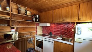 A compact kitchen with wooden cabinets, a red tiled backsplash, and basic appliances.