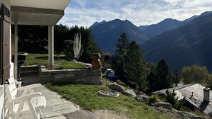 A mountain view from a covered outdoor area with a stone bench and a rustic building.