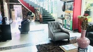 A modern lobby with a staircase, a grey armchair, a black sofa, and a vase with flowers. - Villa Angelia Hotel Annex (Lagos)