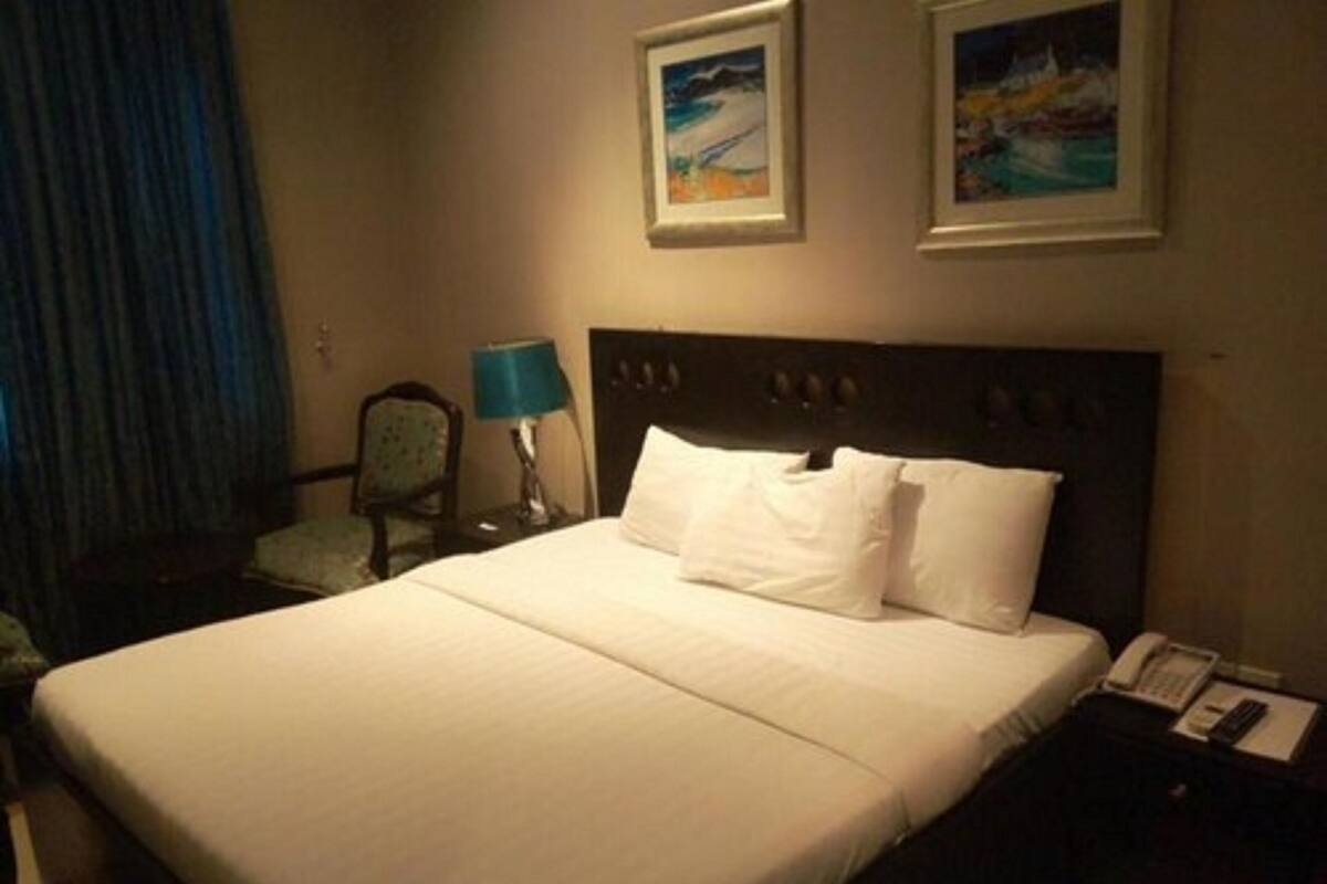A hotel room with a large bed, a nightstand with a telephone, and two framed pictures on the wall.