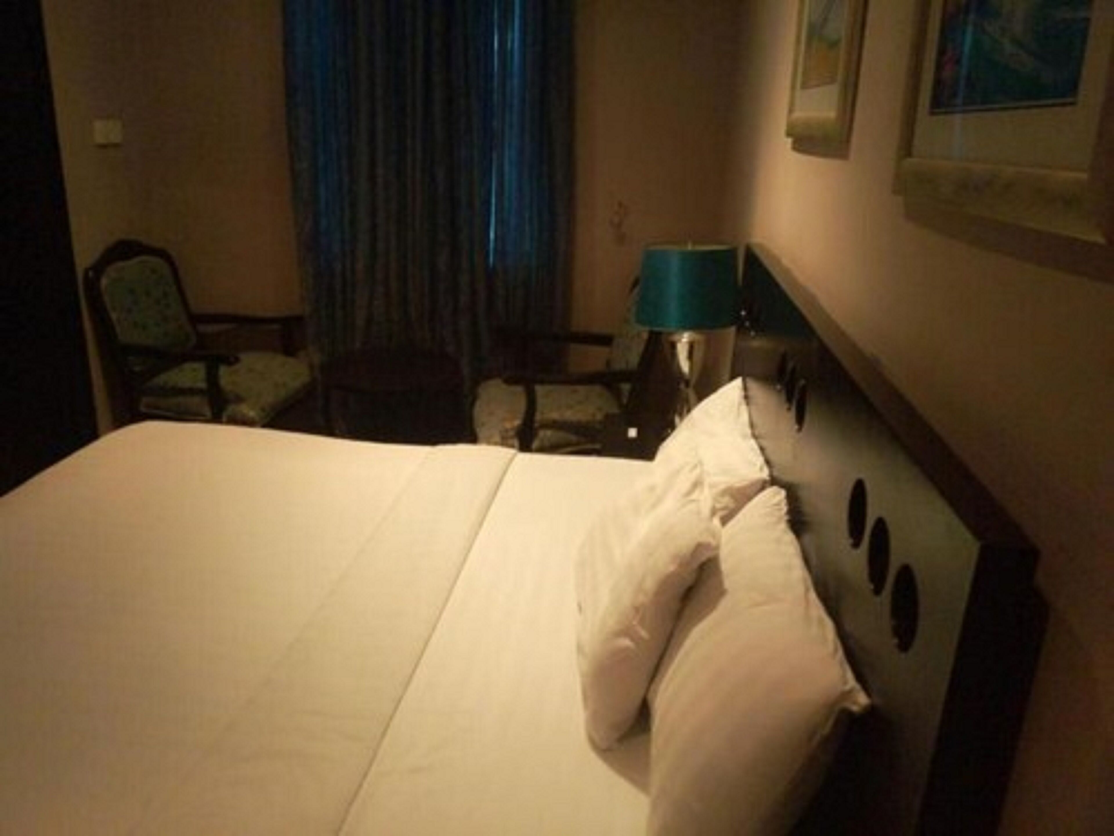 A hotel room with a large bed, a chair, a lamp, and a curtain.