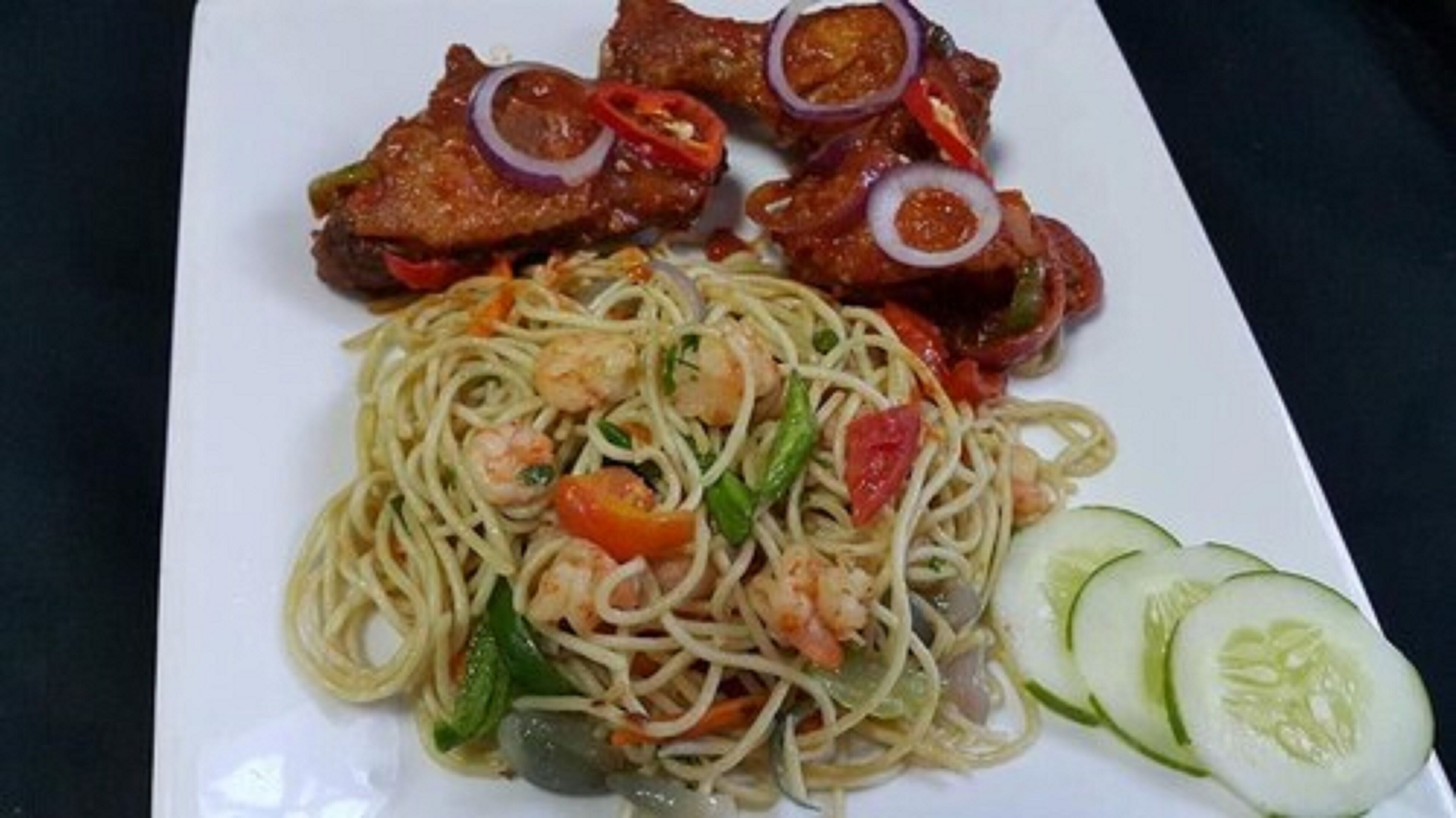 Eine Spaghetti-Platte mit Garnelen und Gemüse, dazu zwei gegrillte Fleischstücke mit roten Zwiebelringen.