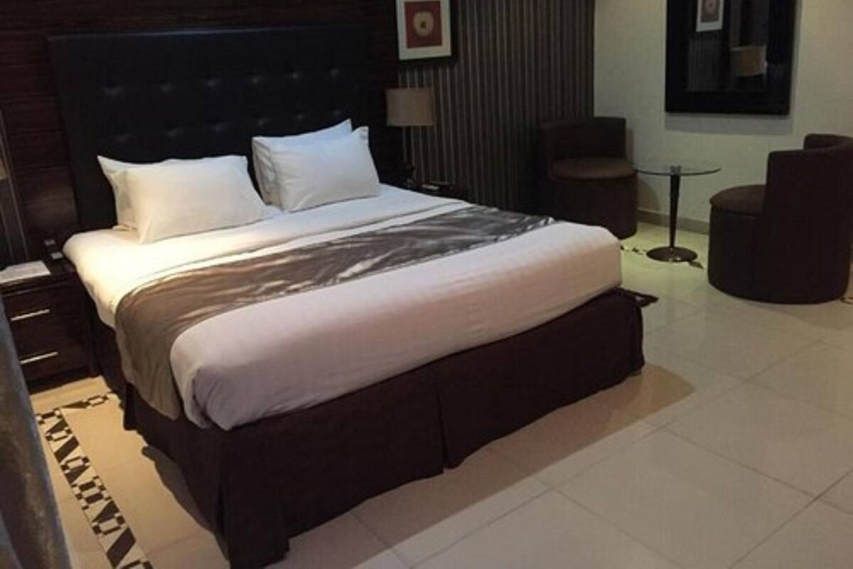 A hotel room with a large bed, a small round table, and a chair.