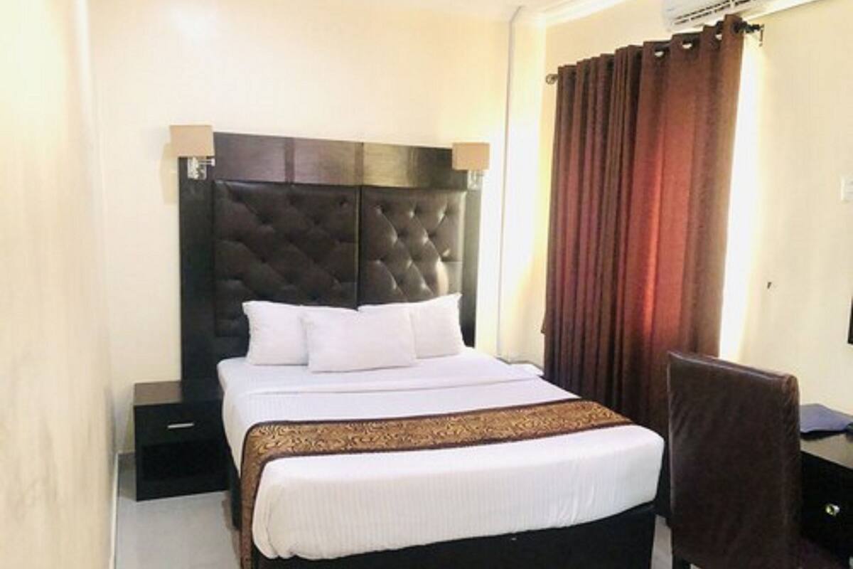 A hotel room with a large bed, a dark headboard, a desk, and a chair.