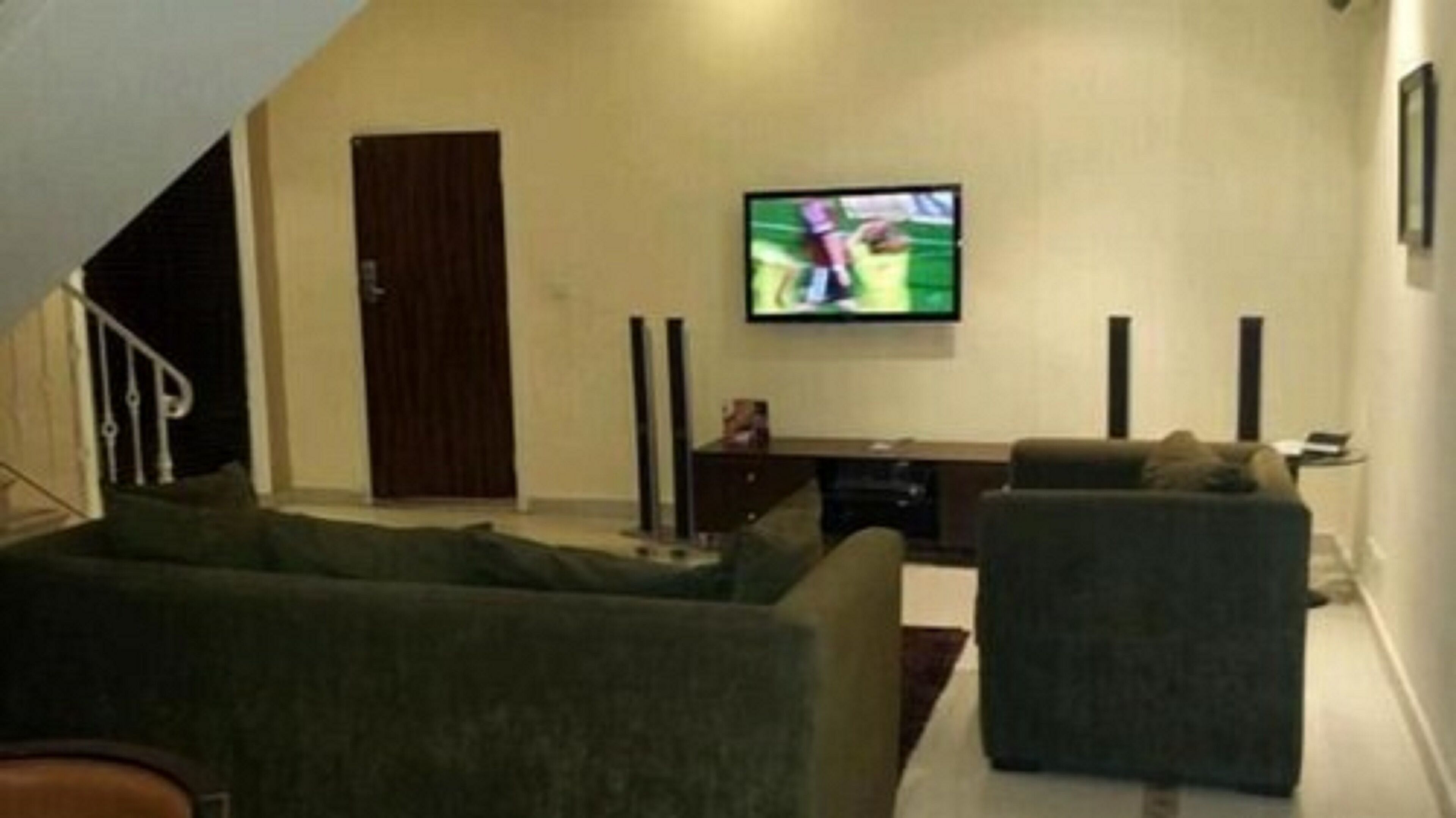 A living room with a flat-screen TV mounted on the wall, a dark-colored sofa, and a staircase leading to another level.