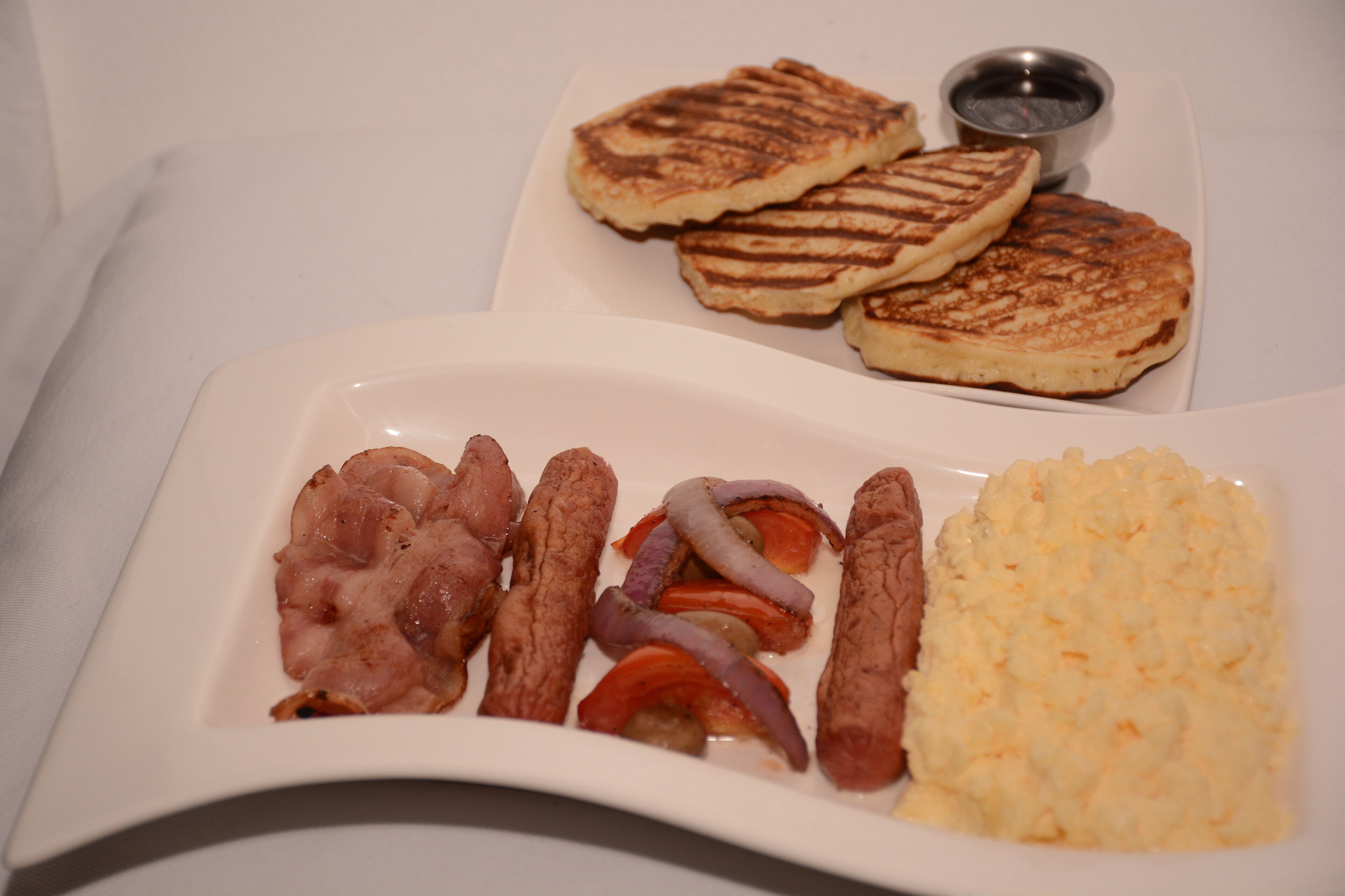 Ein Frühstücksteller mit Speck, Würstchen, gegrillten Tomaten und Rühreiern.