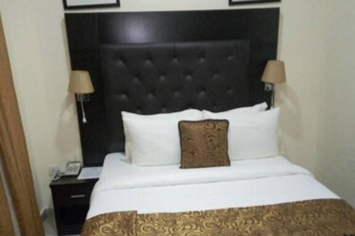 A hotel room with a large bed, a dark headboard, two bedside lamps, and framed artwork on the walls.