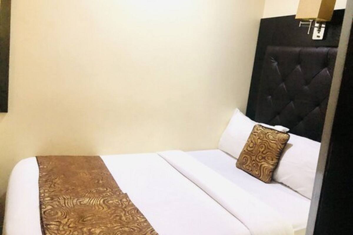 A hotel room with a large bed, a headboard, and a wall-mounted lamp.