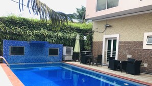 A swimming pool with blue tiles, a tiled deck, and outdoor furniture. - Villa Angelia Hotel Annex (Lagos)