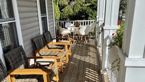 Eine Holzterrasse mit Korbstühlen und einem Tisch, umgeben von weißen Geländern und Grünpflanzen.