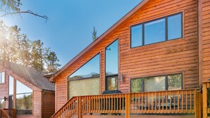 A wooden cabin with a deck, large windows, and a staircase leading to the entrance. - River Rock -- Ev # 3 Bedroom Condo by RedAwning (Estes Park)