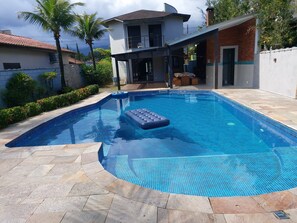 Une piscine dont le bord est recouvert de carreaux bleus, une chaise longue et une maison en arrière-plan.