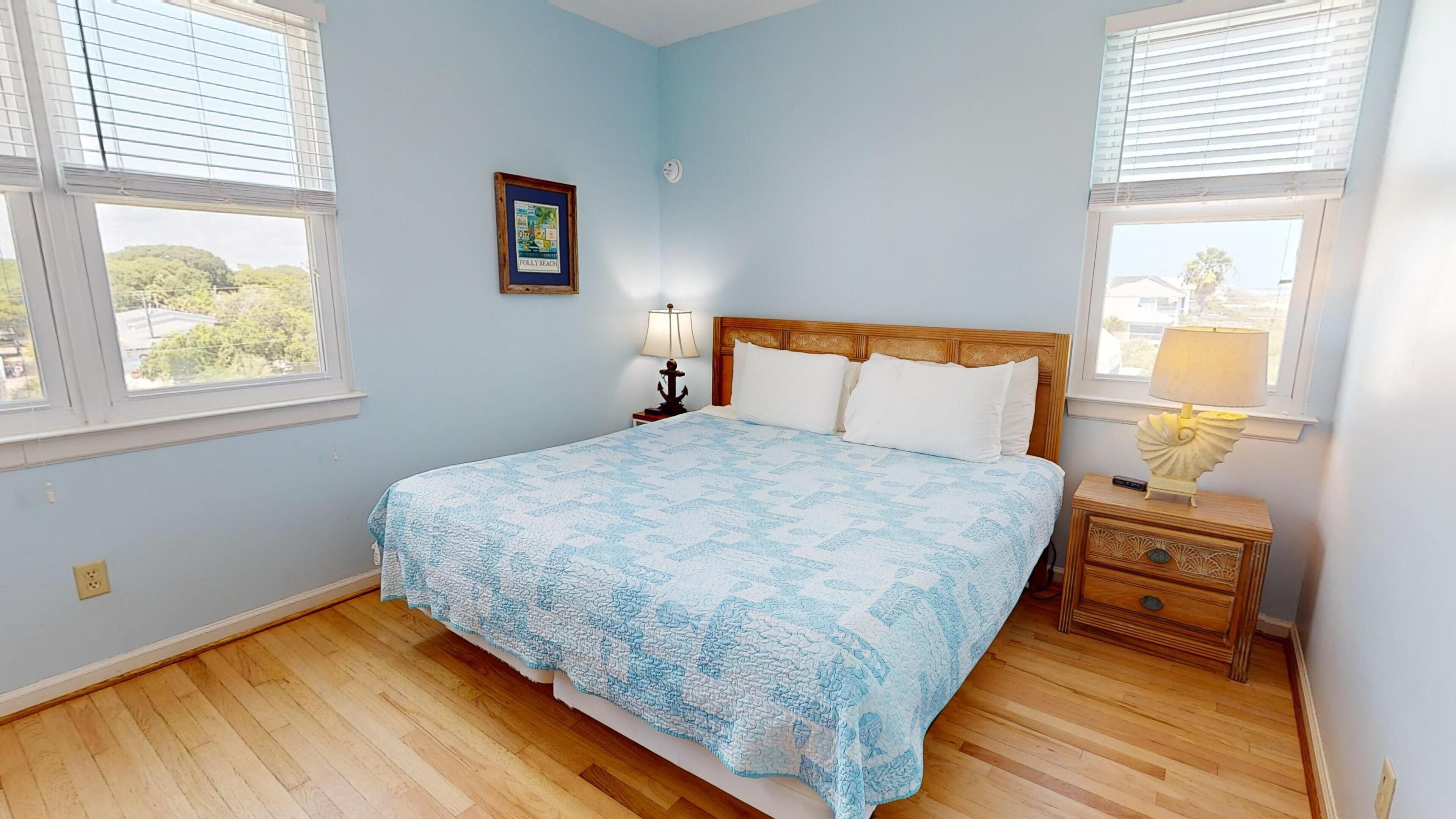 A bedroom with a bed, two bedside tables, a nightstand, a lamp, a framed picture, and a window.