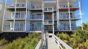 A multi-story beachfront building with balconies, a wooden deck, and a view of the ocean.